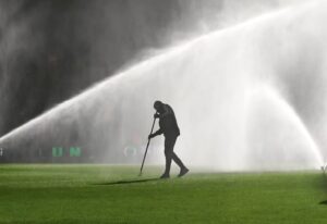 Groundskeeper irrigating a synthetic soccer field before kickoff to reduce surface temperature, improve athlete safety, and cool the artificial turf on a hot day.